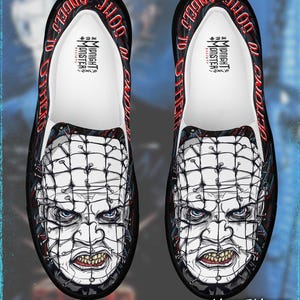 May include: Pair of black slip-on shoes with a graphic of a character's face with pins and a grid pattern. The shoes have the text "ANGELS TO OTHER" and "MIDNIGHT MONSTER". The shoes are a horror-themed product.