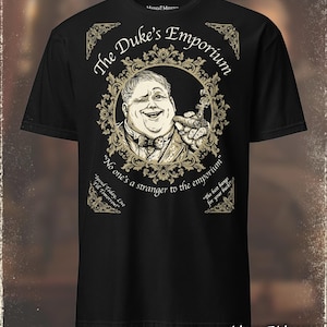 Pode incluir: Camiseta preta com uma ilustração detalhada de um homem com um charuto, emoldurada por detalhes dourados. O texto diz "The Duke's Emporium" e inclui outras frases. O logotipo Midnight Monster está na parte inferior.