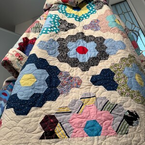 Puede incluir: Un edredón hecho a mano con un estampado floral con varios colores, incluyendo azul, rojo, amarillo y rosa. El edredón tiene un fondo color crema con un diseño acolchado. El estampado floral está hecho de formas hexagonales.