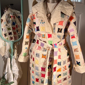 May include: A cream-coloured quilted coat with a colourful patchwork design. The coat features a wrap-around style with a matching belt, large lapels, and rolled cuffs. The patchwork includes squares of various colours and patterns.