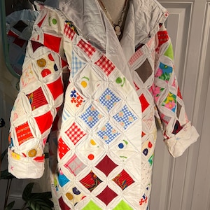 Può includere: Una giacca trapuntata bianca con un design a patchwork. La giacca è realizzata con diversi tessuti di colori diversi, tra cui rosso, blu, verde e rosa. La giacca ha un cappuccio e una manica lunga.