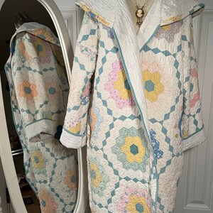 Puede incluir: Una bata blanca acolchada con un patrón floral en tonos de rosa, amarillo y azul. La bata tiene capucha y está forrada con tela blanca.