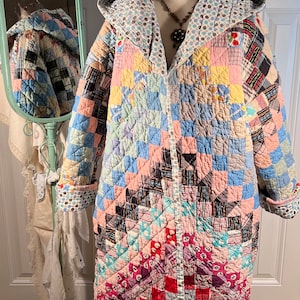 Puede incluir: Una chaqueta vintage de patchwork con capucha. La chaqueta está hecha de varias telas en tonos de rosa, azul, verde y rojo. La colcha está acolchada en forma de diamante.