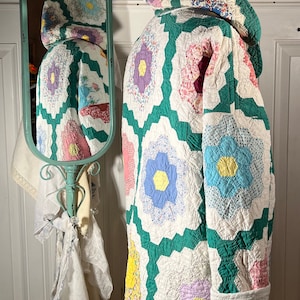 Puede incluir: Una chaqueta acolchada vintage verde y blanca con capucha. La chaqueta está hecha de tela de patchwork con diseños florales en tonos de rosa, azul, amarillo y morado.