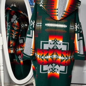 May include: A green hooded robe with a geometric pattern in shades of red, orange, white, and gray. The robe is made of a soft, fuzzy material and has a long, flowing design.