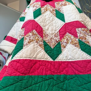 Könnte beinhalten: Eine handgefertigte Steppdecke mit Patchwork-Design. Die Steppdecke hat eine Kombination aus rotem, grünem, weißem und gemustertem Stoff. Die Steppdecke hat eine gesteppte Textur und eine Kapuze. Das Gesamtdesign ist geometrisch und die Steppdecke scheint Vintage zu sein.