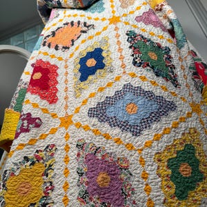 Puede incluir: Una colcha vintage con un diseño de patchwork que presenta una variedad de patrones florales en tonos de rojo, azul, amarillo, verde y morado. La colcha está acolchada con hilo amarillo en un patrón de diamante.