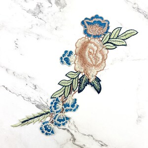 May include: A delicate floral embroidery patch featuring a large pink rose with blue and green accents. The patch is perfect for adding a touch of vintage charm to clothing, bags, or home decor projects.