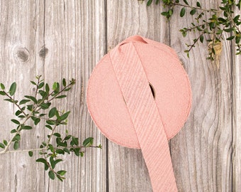 May include: A roll of pink fabric ribbon with a textured surface. The ribbon is rolled up and tied with a bow.