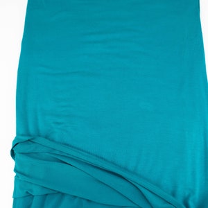 May include: A teal blue fabric with a smooth texture. The fabric is folded and draped, showing its soft and flowing nature.