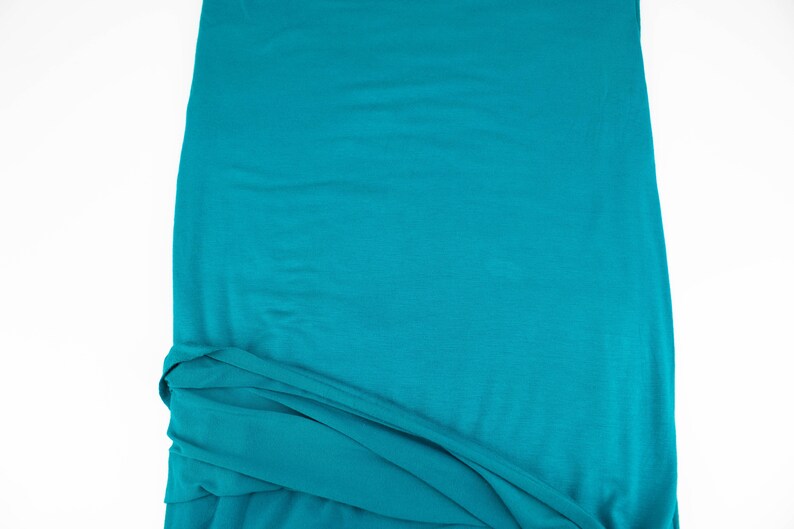 May include: A teal blue fabric with a smooth texture. The fabric is folded and draped, showing its soft and flowing nature.