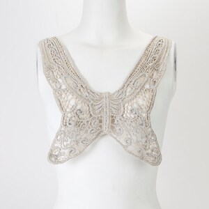 May include: A delicate, off-white lace butterfly-shaped neckline trim. The trim is made of a fine, openwork lace with a subtle shimmer.