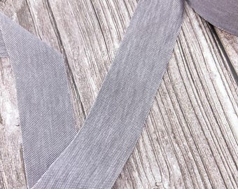 May include: A roll of gray elastic trim with a textured surface. The trim is lying on a wooden surface.