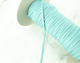 May include: A spool of light blue cord or string wound around a cardboard core. The cord is smooth and has a subtle sheen.