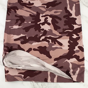 May include: A piece of camouflage fabric folded in half, revealing the reverse side. The fabric is a light brown with dark brown and black camouflage patterns.