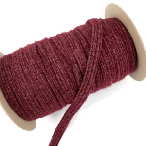 May include: A spool of burgundy red knitted elastic cord. The cord is wound around a cardboard spool.