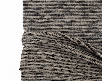 May include: Close-up of a black and beige striped fabric with a soft, fuzzy texture. The fabric is folded over, revealing the underside, which is a similar striped pattern but with a slightly different texture.
