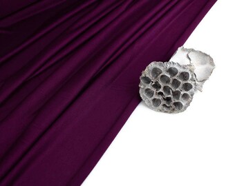 May include: A close-up of a dried lotus pod on a white background. The pod is light brown and has a honeycomb-like texture. A deep purple fabric is draped in the background.