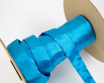 May include: A spool of bright turquoise satin ribbon. The ribbon is neatly wound around a cardboard core, with a length of the ribbon extending outwards. The ribbon has a smooth, shiny texture, and the color is a vibrant, solid turquoise.