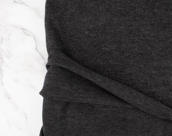 May include: Close-up of a dark gray fabric with a textured surface. The fabric is folded and draped, showing the soft, drapey texture.