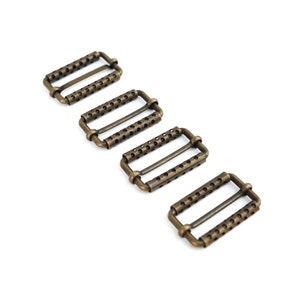 May include: Four antique bronze rectangular slider buckles with a series of small holes and a central bar. These metal hardware pieces are ideal for straps, belts, or other crafting projects. The buckles are arranged diagonally on a white background.