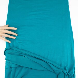 May include: A teal blue fabric with a smooth texture. The fabric is folded and draped over a white surface.