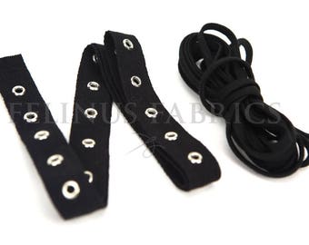 May include: Black fabric strips with silver eyelets and a black cord. The strips are arranged in a zig-zag pattern, and the cord is coiled. The eyelets are evenly spaced along the strips.