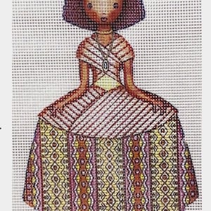 May include: A needlepoint pattern of a girl with brown hair wearing a yellow and brown dress with a geometric pattern. The girl is sitting with her hands in her lap.