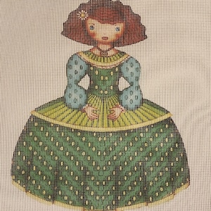 May include: A needlepoint doll with red hair, a green and blue dress with white polka dots, and a yellow flower in her hair.