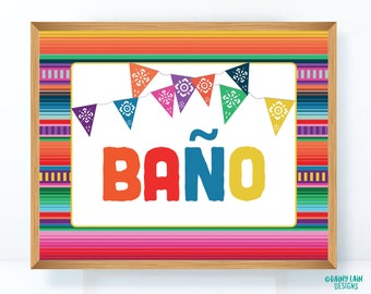 May include: A colorful sign with a white background and the word "BAÑO" in large, colorful letters. The sign is decorated with a string of colorful pennants with floral designs. The sign is framed in a wooden frame with a colorful striped border.