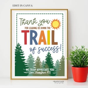 May include: A framed print with the text "Thank you for leading us down the trail of success!" in various colors. The image includes a sun illustration and a forest scene at the bottom. A small potted plant in a red pot is on the right.