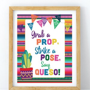 May include: A framed print with a colorful Mexican fiesta theme. The text reads "Grab a PROP, Strike a POSE, Say QUESO!" with a cactus illustration. The background features a vibrant striped pattern and decorative pennants.