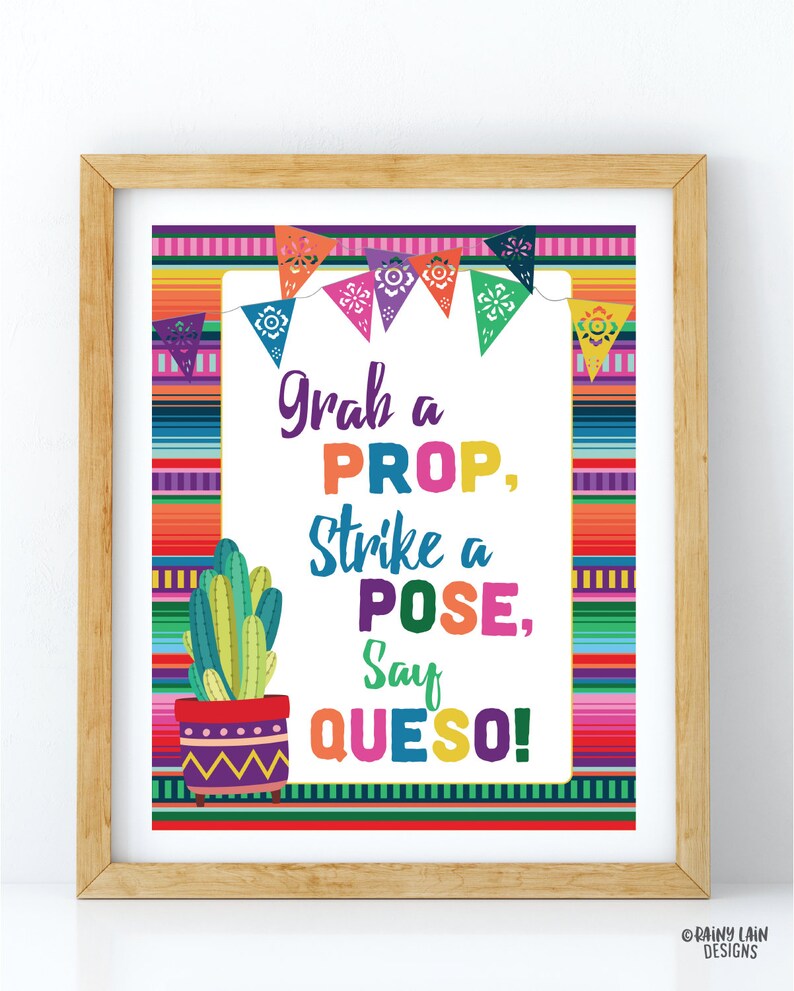 May include: A framed print with a colorful Mexican fiesta theme. The text reads "Grab a PROP, Strike a POSE, Say QUESO!" with a cactus illustration. The background features a vibrant striped pattern and decorative pennants.