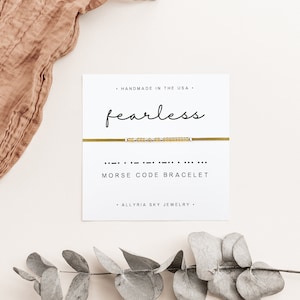Peut inclure: Un bracelet en or avec le mot "fearless" écrit en code Morse. Le bracelet est présenté sur une carte blanche avec les mots "Handmade in the USA", "Morse Code Bracelet", et "Allyria Sky Jewelry".