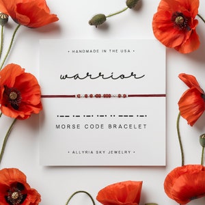 May include: Red and silver beaded bracelet with the word "warrior" written in cursive above it. The bracelet is displayed on a white card with the text "Morse Code Bracelet" and "Handmade in the USA" written below it.
