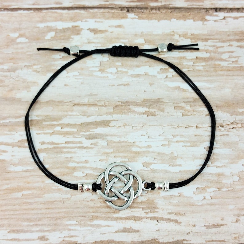 May include: A black cord bracelet with a silver Celtic knot charm and silver beads.