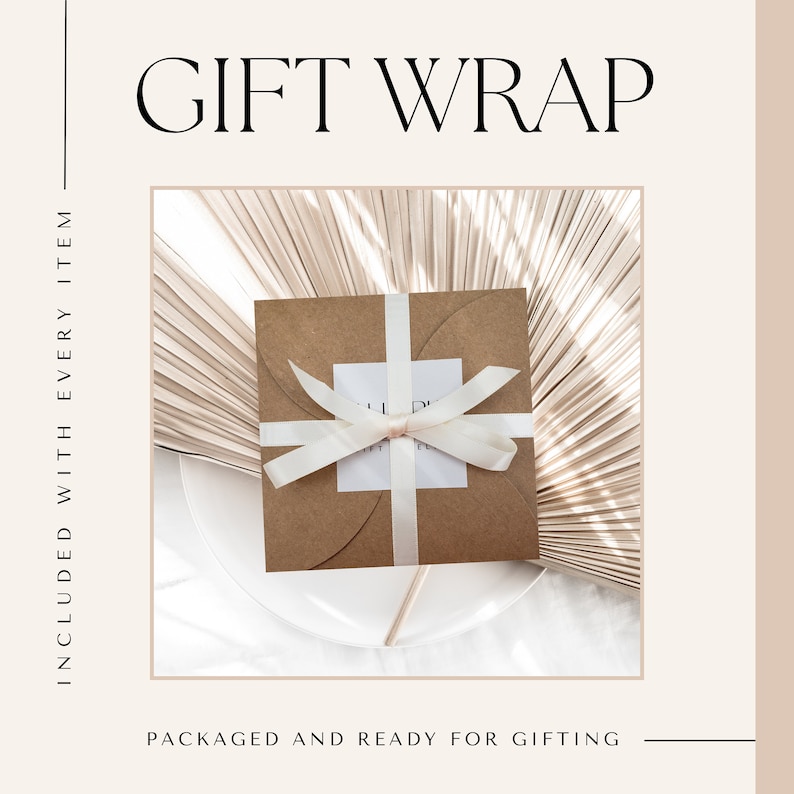 May include: A brown paper gift box with a white satin ribbon tied in a bow. The box is sitting on a white surface with a light brown palm leaf background.