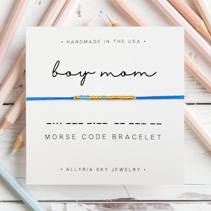 May include: A blue and gold beaded bracelet with the words "boy mom" and "Morse Code Bracelet" on a white card. The card also says "Handmade in the USA" and "Allryia Sky Jewelry".