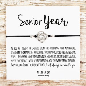 May include: A black leather bracelet with a silver Celtic knot charm and a card that reads "Senior Year" with a message of encouragement for a graduate. The card reads, "As you get ready to embark upon this exciting new adventure, remember to dream big, work hard, surround yourself with awesome people, and make some amazing new memories. Most importantly, never forget that I will be here cheering you on every step of the way. Even though I can't be there with you, I will always be here for you." The card is signed "Allyria Sky, Boho Glam Jewelry."