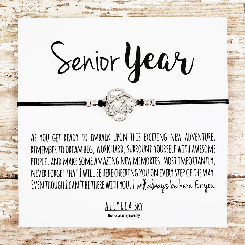May include: A black leather bracelet with a silver Celtic knot charm and a card that reads "Senior Year" with a message of encouragement for a graduate. The card reads, "As you get ready to embark upon this exciting new adventure, remember to dream big, work hard, surround yourself with awesome people, and make some amazing new memories. Most importantly, never forget that I will be here cheering you on every step of the way. Even though I can't be there with you, I will always be here for you." The card is signed "Allyria Sky, Boho Glam Jewelry."
