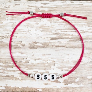 May include: A pink string bracelet with silver beads and white beads with the number 5 on them.