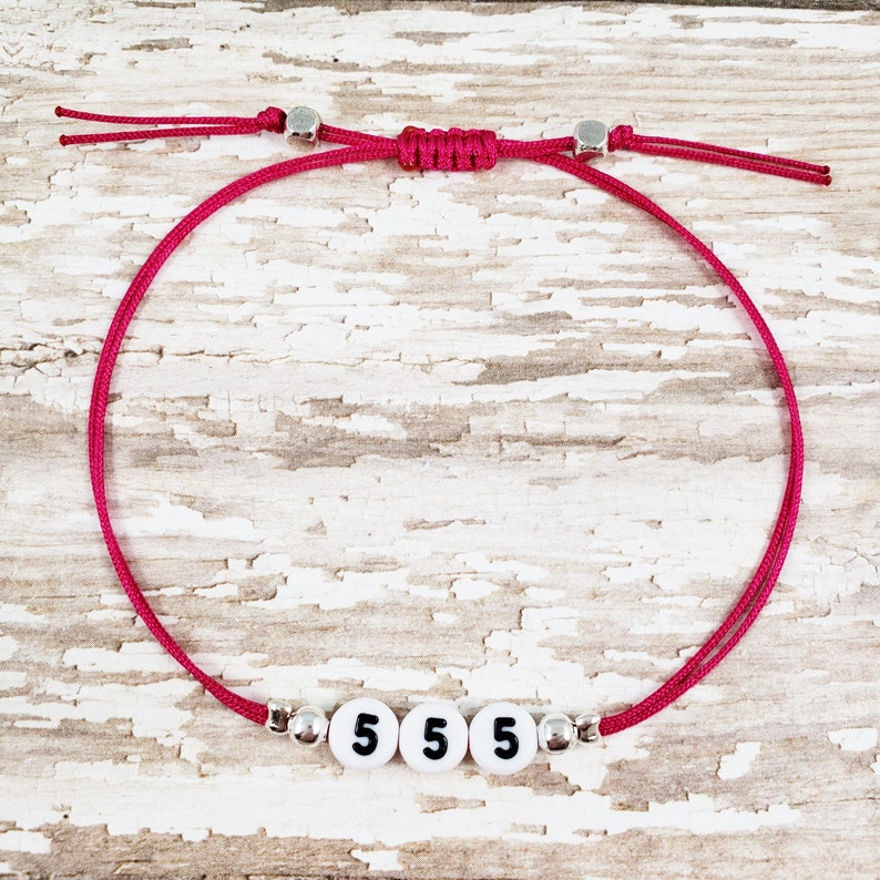 May include: A pink string bracelet with silver beads and white beads with the number 5 on them.