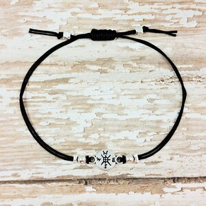 May include: A black cord bracelet with silver beads and a compass charm. The compass charm has the letters N, S, E, and W engraved on it.