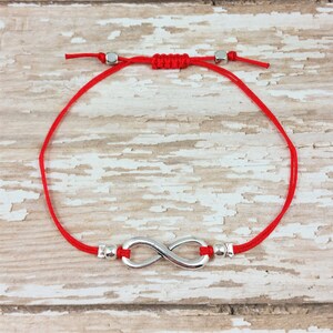 May include: Red string bracelet with a silver infinity symbol charm and silver beads.