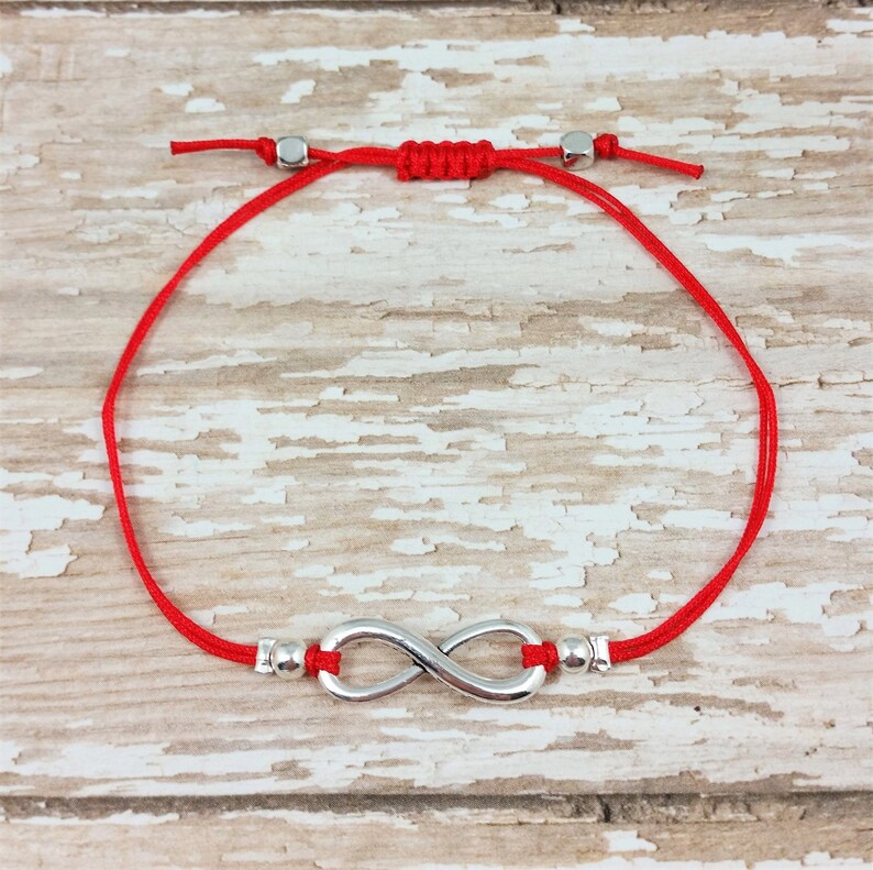 May include: Red string bracelet with a silver infinity symbol charm and silver beads.