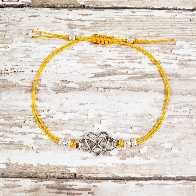 May include: A yellow cord bracelet with a silver infinity heart charm and silver beads.
