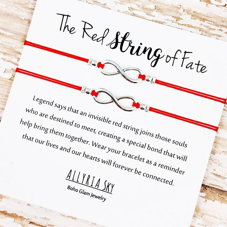 May include: Two red string bracelets with silver infinity charms. The card reads "The Red String of Fate" and explains the legend of the red string of fate.