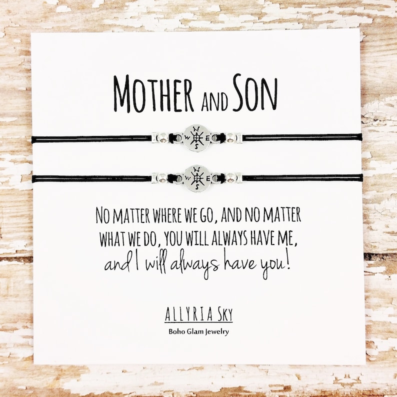 May include: A white card with black text that reads "Mother and Son" and "No matter where we go, and no matter what we do, you will always have me, and I will always have you!"  The card also includes the text "ALLYRIA SKY" and "Boho Glam Jewelry". Two black bracelets with compass charms are displayed on the card.