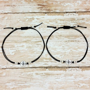 May include: Two black cord bracelets with silver compass charms. The charms have the letters N, S, E, and W on them.