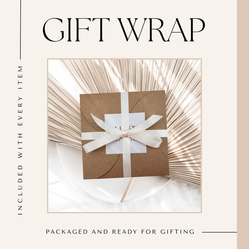 May include: A brown paper gift box with a white satin ribbon tied in a bow. The box is sitting on a white surface with a light brown palm leaf background.